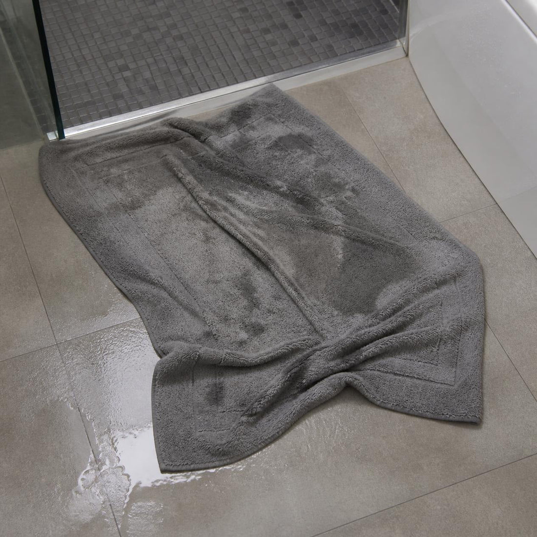 Worn traditional cotton bath mat with frayed edges sitting on a bathroom tile floor.