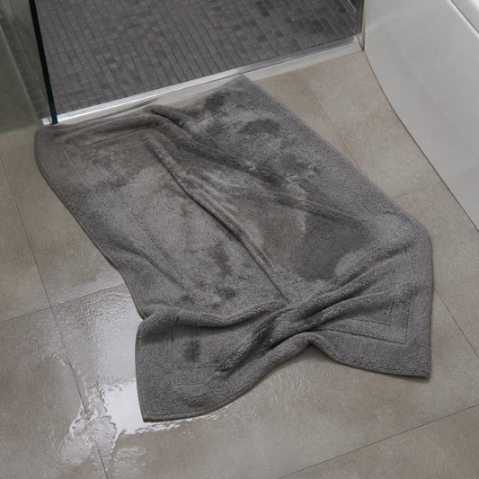 Worn traditional cotton bath mat with frayed edges sitting on a bathroom tile floor.