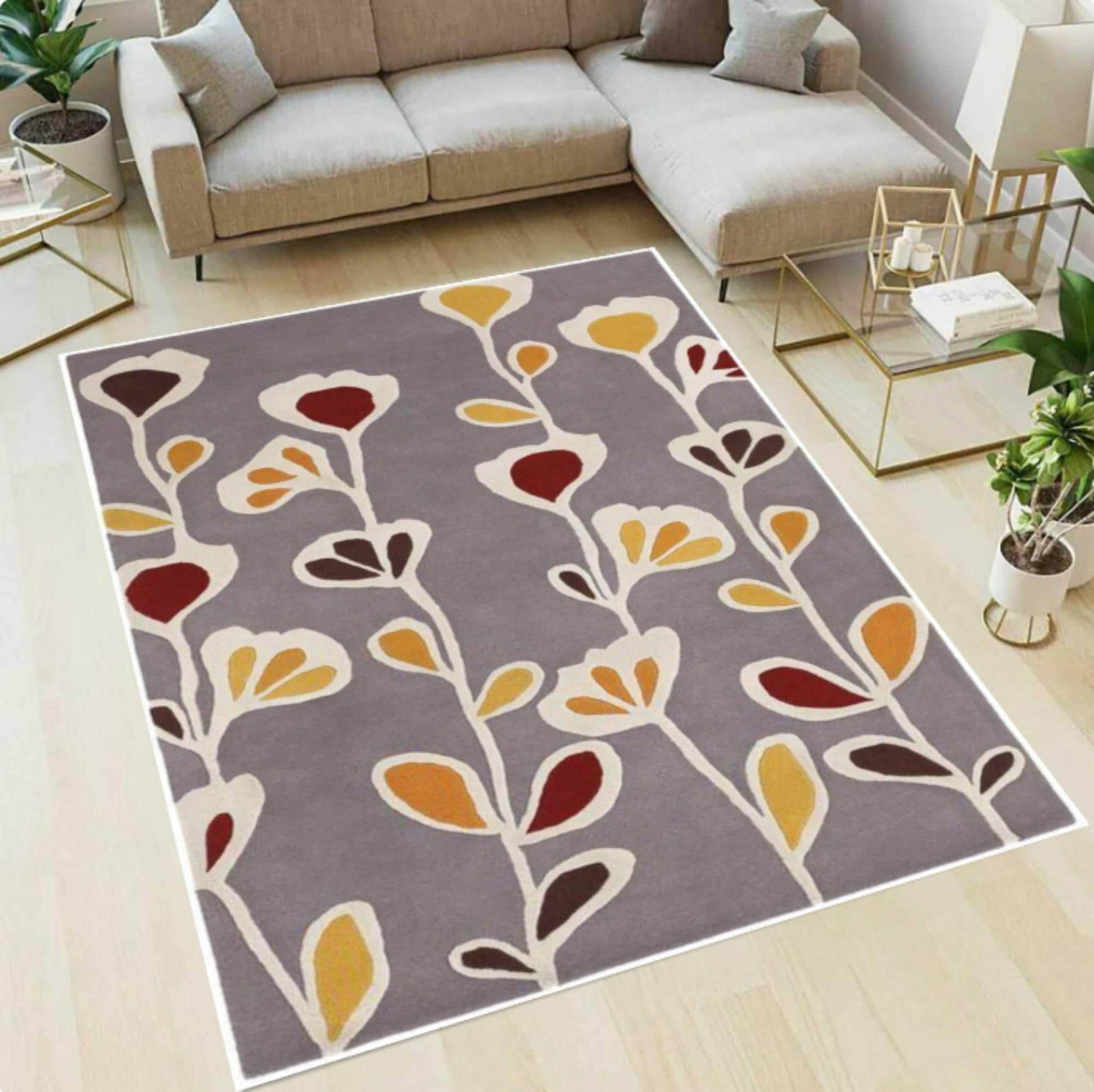 A rectangular area rug with a modern botanical pattern featuring cream, mustard yellow, and burgundy leaves on a taupe-gray background, styled in a bright living room next to a beige sectional sofa.