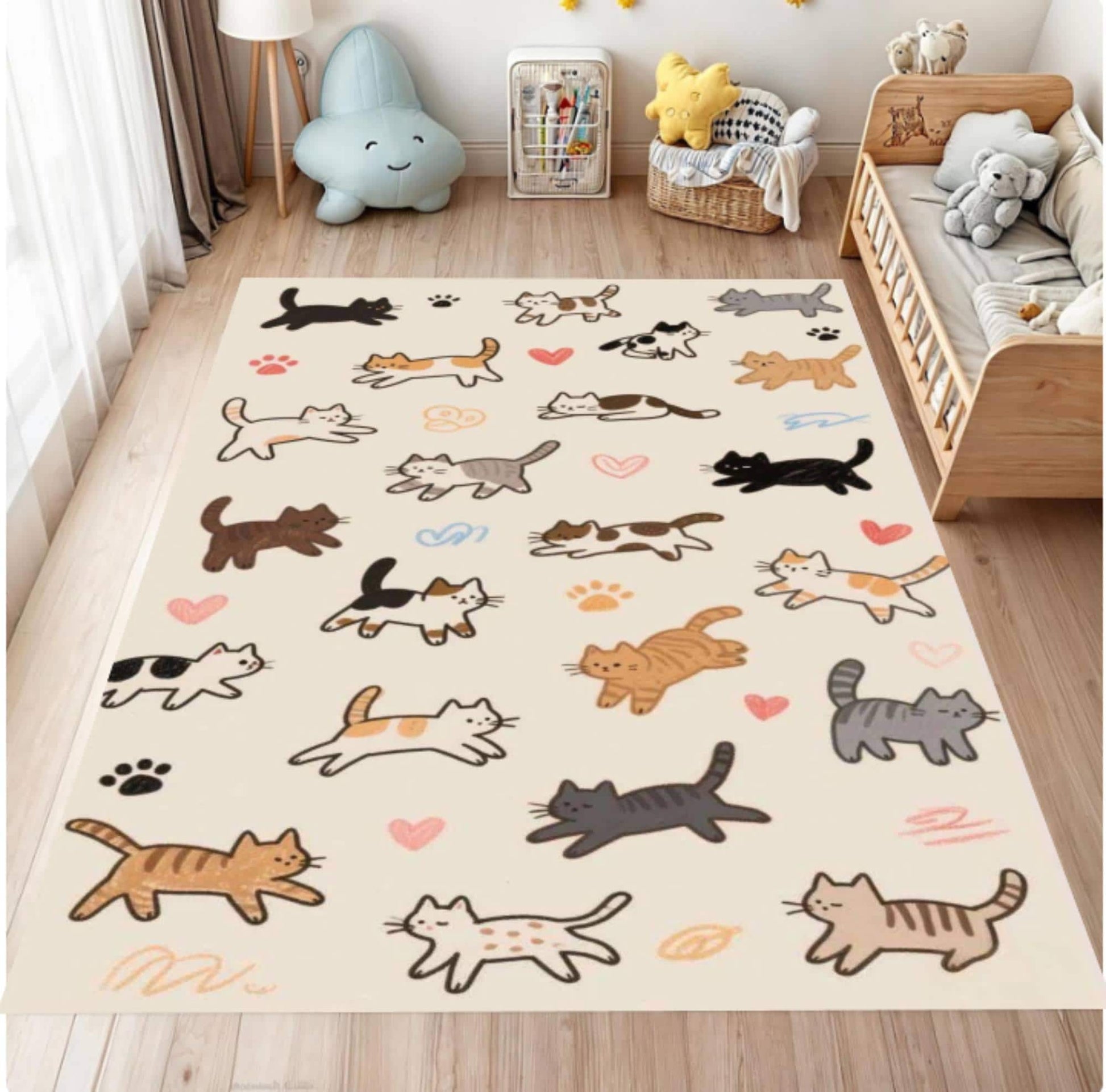 A rectangular cream-colored area rug with a playful pattern of cartoon cats, paw prints, and small hearts, displayed on a light wood floor in a child's bedroom next to a wooden bed.