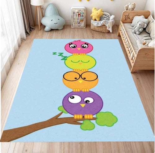 A rectangular area rug with a light blue background and a cartoon stack of four colorful owls perched on a branch, shown in a children's bedroom setting.