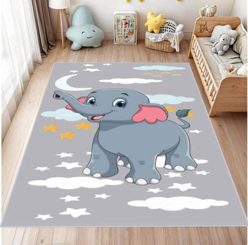 A gray children's area rug featuring a cartoon gray elephant with pink ears, white clouds, and yellow stars, shown on a light wood floor in a styled nursery room.