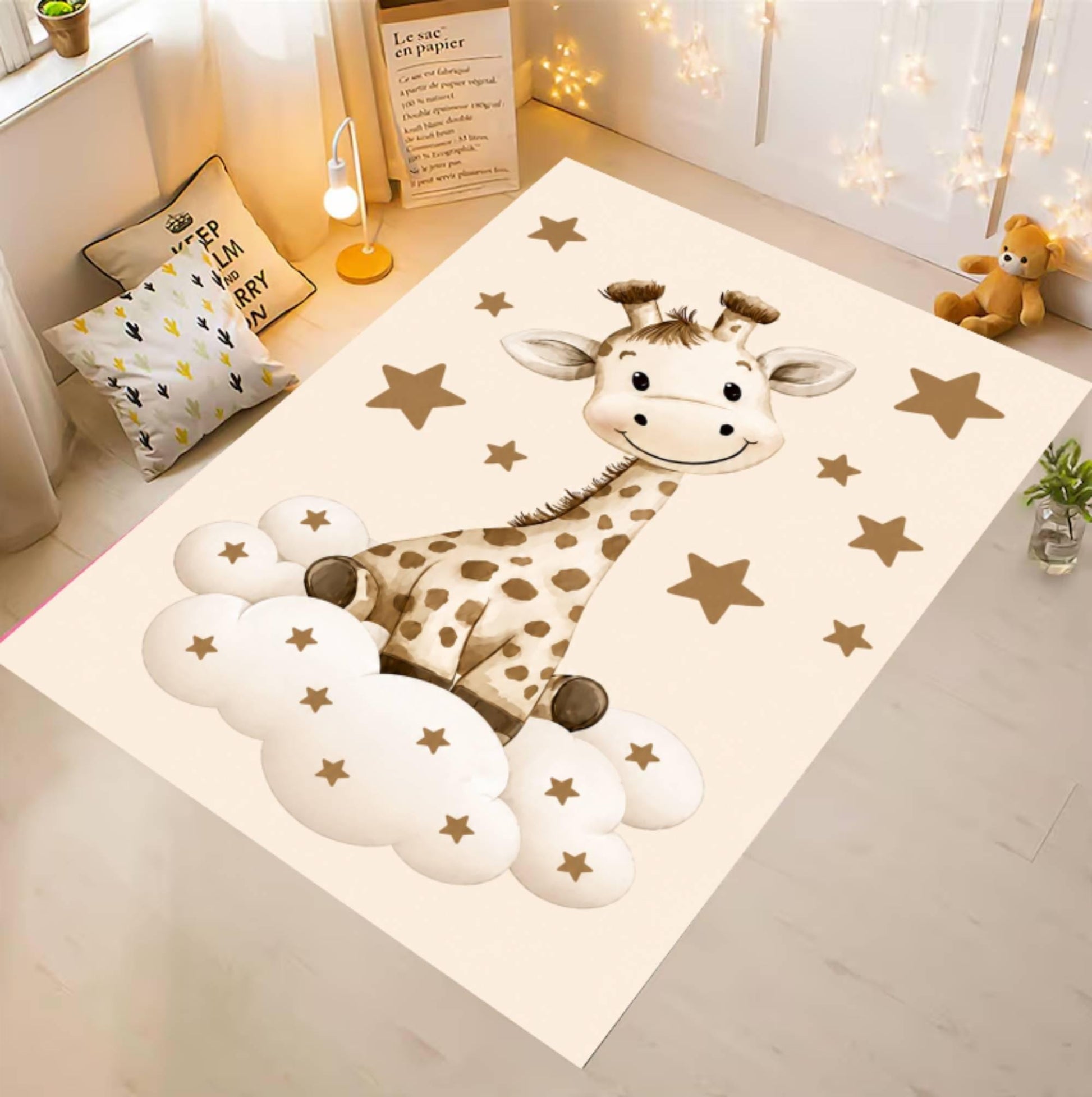 A rectangular cream rug or play mat laid on a light floor in a styled room, featuring a cartoon giraffe sitting on white clouds with scattered gold stars. The room includes pillows, a small lamp, a teddy bear, and string lights in the background.