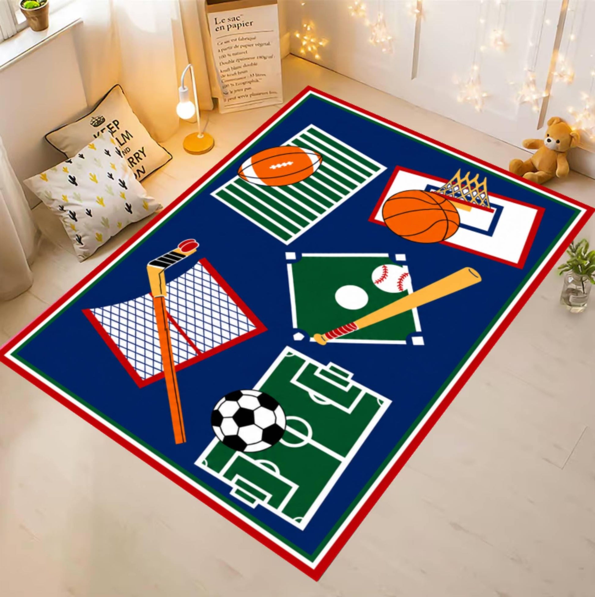 A rectangular area rug with a sports theme, featuring a navy blue background with red and white borders and illustrations of various sports equipment like a football, basketball, soccer ball, baseball bat, and hockey stick. The rug is displayed in a child's bedroom setting on a light wood floor.