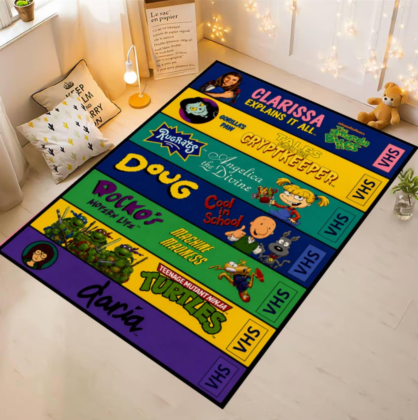A rectangular floor mat or rug featuring colorful Teenage Mutant Ninja Turtles VHS-style panels, shown laid out on a light wood floor in a styled room with pillows, a lamp, string lights, and a teddy bear.