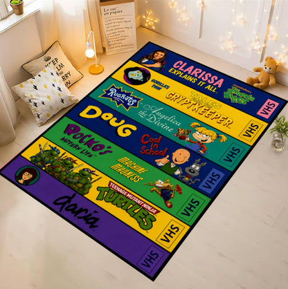 A rectangular floor mat or rug featuring colorful Teenage Mutant Ninja Turtles VHS-style panels, shown laid out on a light wood floor in a styled room with pillows, a lamp, string lights, and a teddy bear.