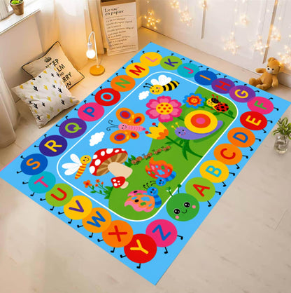 A colorful children's alphabet play mat rug displayed on a light wood floor in a styled room. The rug features a bright blue border with alphabet letters in circular shapes and a green center depicting a whimsical garden with flowers, butterflies, and animals.