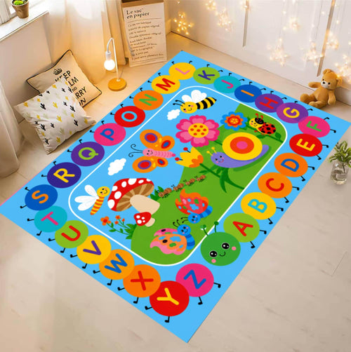 A colorful children's alphabet play mat rug displayed on a light wood floor in a styled room. The rug features a bright blue border with alphabet letters in circular shapes and a green center depicting a whimsical garden with flowers, butterflies, and animals.