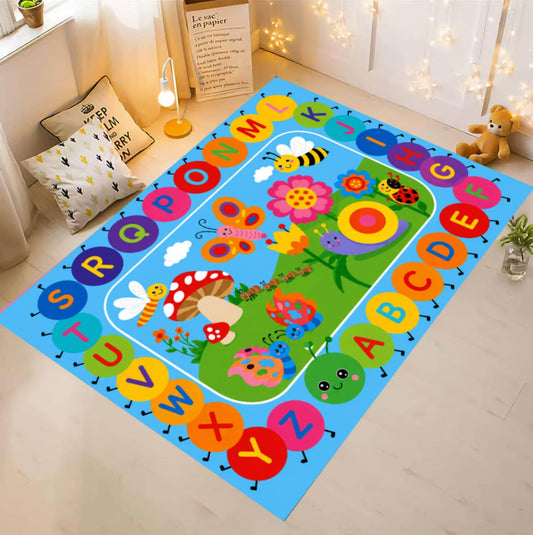A colorful children's alphabet play mat rug displayed on a light wood floor in a styled room. The rug features a bright blue border with alphabet letters in circular shapes and a green center depicting a whimsical garden with flowers, butterflies, and animals.