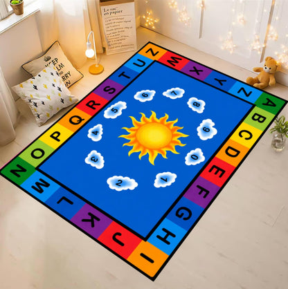 A colorful children's area rug laid on a light wood floor in a styled room. The rug has a bright blue center with a yellow sun and white clouds, surrounded by a rainbow border with alphabet letters and numbers.