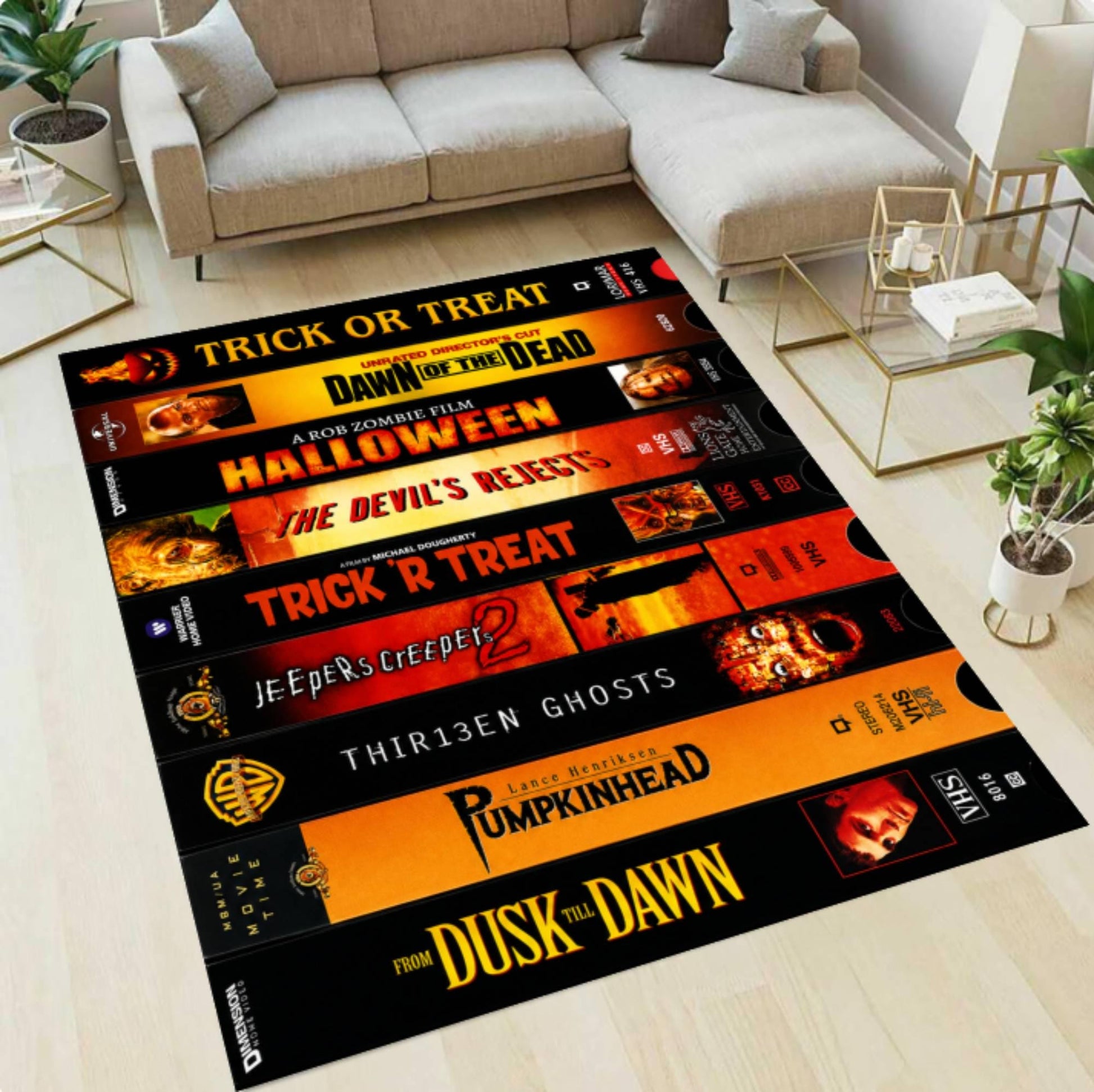 A rectangular area rug featuring a collage of horror movie posters in black, orange, yellow, and red tones, styled on a light wood floor in a modern living room with a sofa and side tables.