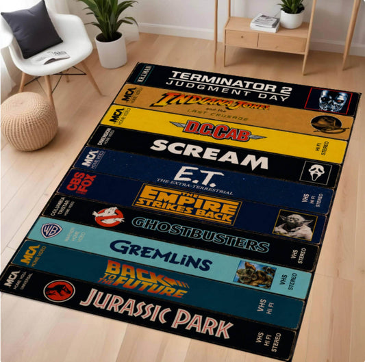 A long rectangular area rug laid on a light wood floor in a styled room, featuring stacked VHS tape designs with pop culture movie and franchise graphics including Terminator 2, Alien, Scar, Scream, E.T.